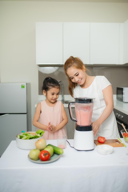 Madre ayudando a su hija a preparar jugo en la cocina de casa