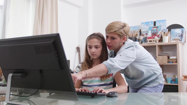 Madre ayudando a su hija con la tarea escolar analizando la lección de matemáticas juntos usando una plataforma académica de aprendizaje electrónico sentada en el escritorio. Niños pequeños estudiando literatura. Educación a distancia