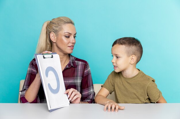 Foto madre ayudando a su hijo con la tarea sobre fondo rosa aislado. educación a distancia.