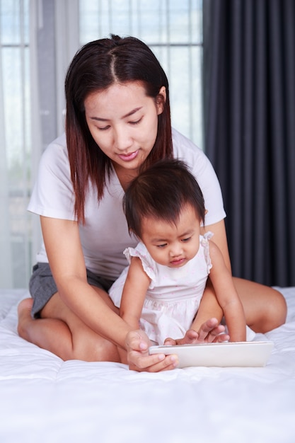 La madre y el bebé buscan jugar y leer la tableta en casa