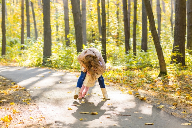 La madre y el bebé de familia feliz ríen con hojas en otoño de la naturaleza