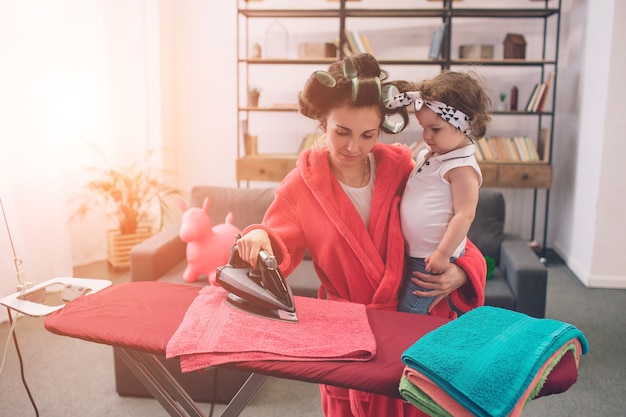 Madre y bebé juntos dedicados a las tareas del hogar Planchado de ropa. Ama de casa y niño haciendo los deberes