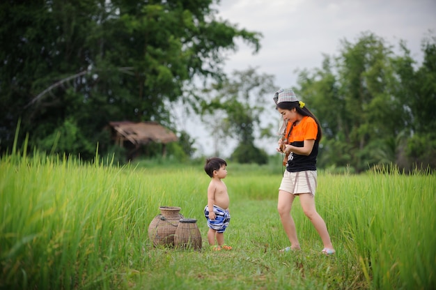 Madre y bebé lindo que juegan en el campo verde del arroz, concepto del amor de la familia.