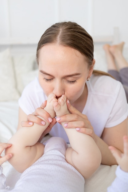 Madre besa los pies del bebé y los huele en la cama de su casa, feliz maternidad