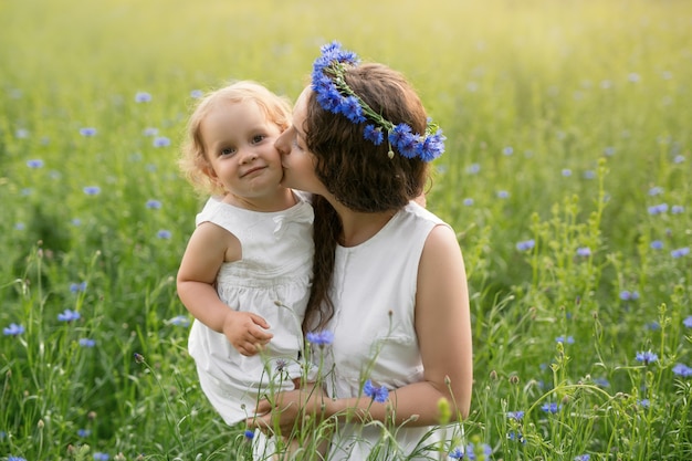 Una madre besa a su hija en un campo de acianos al atardecer