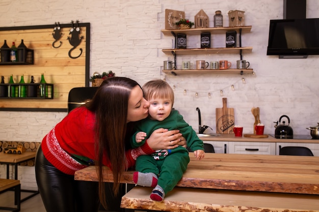 Madre besando a su bebé en la cocina de Navidad en casa