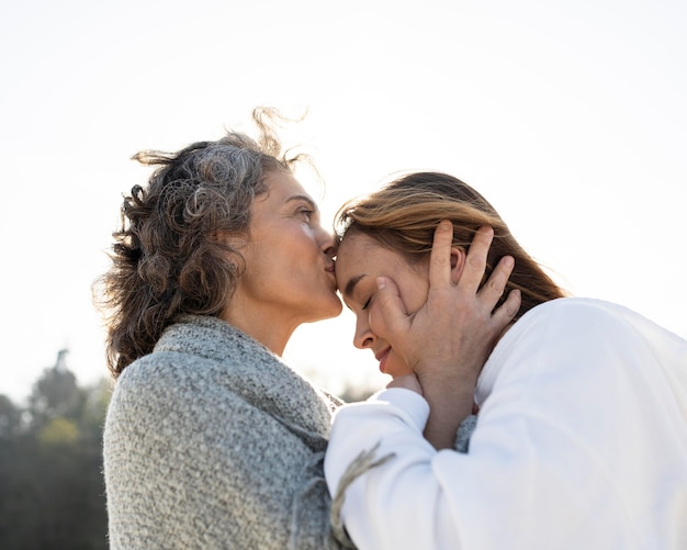 Madre besando a su hija en la frente al aire libre