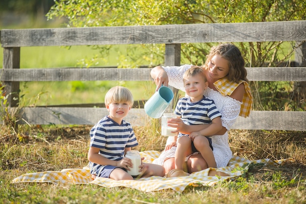 Madre bonita joven que tiene comida campestre con sus niños pequeños. Familia bebiendo leche al aire libre