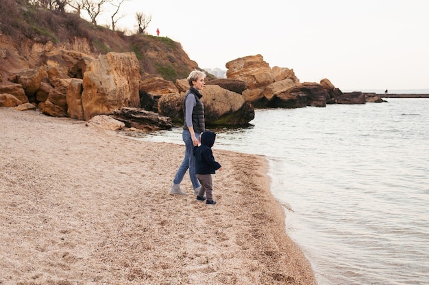 Madre camina con un hijo pequeño cerca del mar en otoño