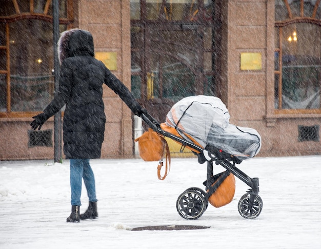 La madre camina con el niño en el cochecito en un día nevado de invierno. Desenfoque de movimiento intencional. Imagen desenfocada