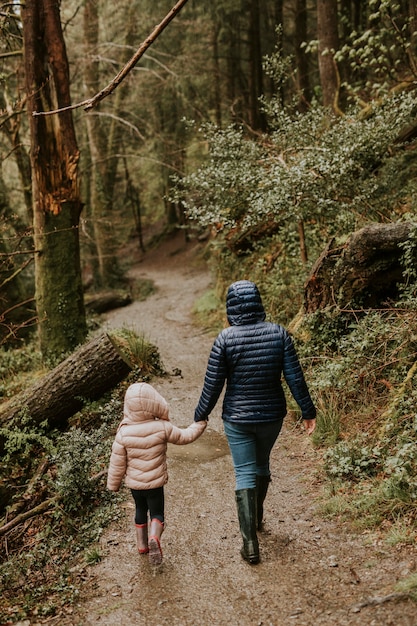 Madre caminando con su hija en la vista trasera del bosque