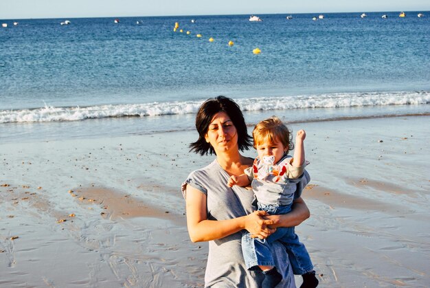 Foto madre cargando a su hijo mientras está de pie en la playa