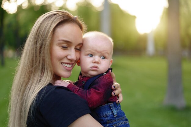 Madre cargando a su lindo hijo en el parque durante la puesta de sol