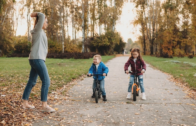 Madre caucásica dando el comienzo a sus hijos que andan en bicicleta en un soleado día de otoño