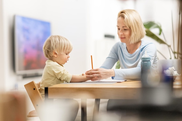 Foto madre caucásica joven y hijo pequeño dibujando pintura en el cuaderno en casa juntos madre amorosa