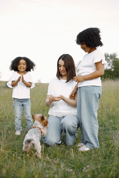 Madre caucásica y sus dos hijas afroamericanas alimentando a un perro al aire libre