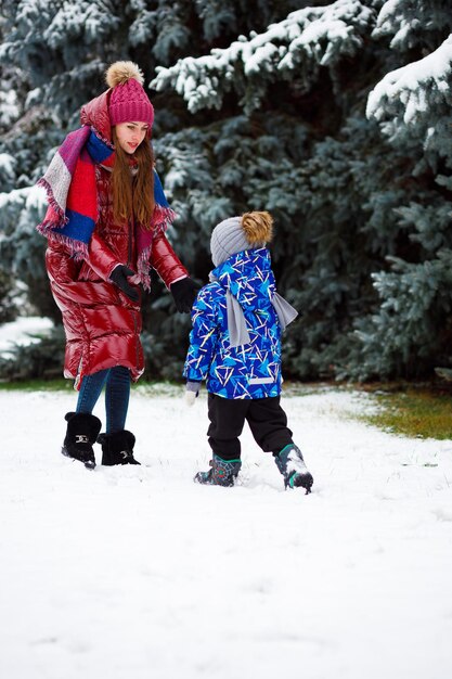 Una madre con una chaqueta roja abraza a su hijo en invierno en un bosque con mucha nieve Año Nuevo 2023