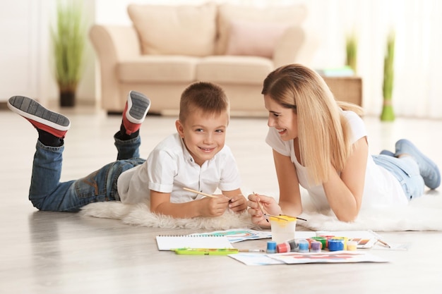 Madre con un chico lindo pintando un cuadro en una hoja de papel en el interior