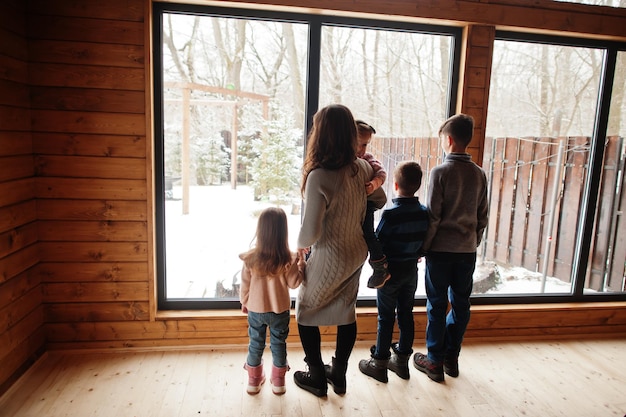 Madre y cuatro hijos en una casa de madera moderna contra una ventana grande