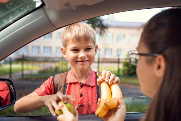 La madre le da frutos a su hijo sonriente a través de la ventanilla del coche