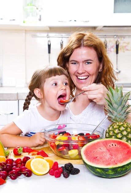 La madre le da a la niña una ensalada de frutas en la cocina.