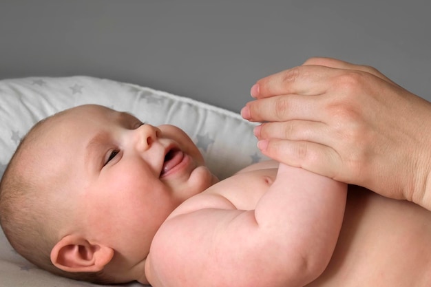 Madre dando masaje a niño pequeño Primer plano Mamá da masaje a bebé infantil Prevención de temblor Manos femeninas masajeando suavemente a recién nacido Cuerpo desnudo Frotis con crema Concepto de cuidado corporal