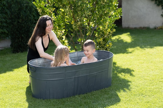 Madre divirtiéndose con niños en una bañera al aire libre en el patio trasero en verano