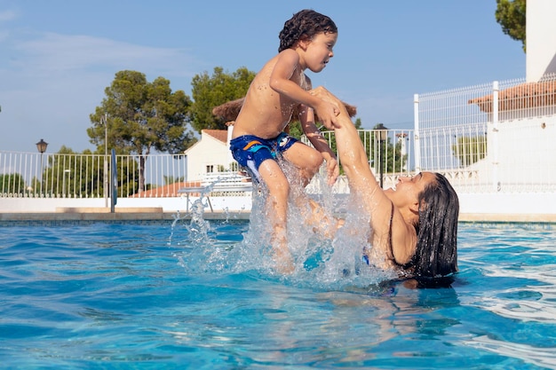 Madre divirtiéndose con su hijo tirándolo a la piscina