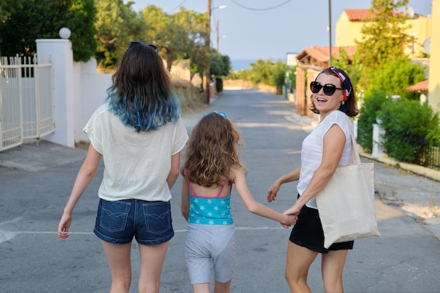 Madre y dos hijas adolescente y más joven caminando juntos tomados de la mano