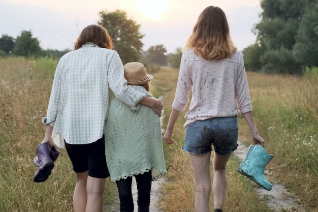 Madre y dos hijas caminando juntas por el camino rural