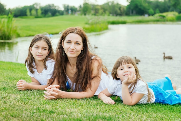 Madre con dos hijas pequeñas se encuentran en la hierba verde en el parque cerca del lago