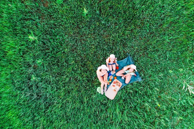 Madre y dos hijas tienen un picnic con pizza en una vista superior aérea de hierba verde