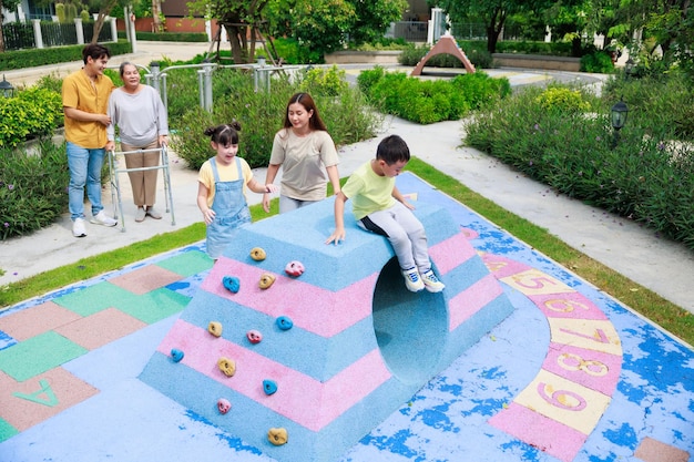 La madre y los dos niños se divierten corriendo juntos mientras el padre y la abuela los buscan para jugar en el patio de recreo