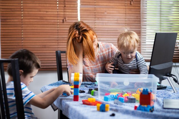 Madre con dos niños pequeños de rodillas intenta reírse en casa.