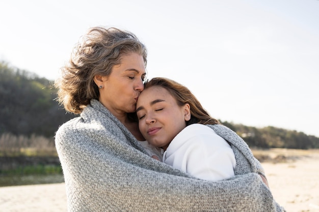 Foto madre e hija abrazándose al aire libre en la playa.