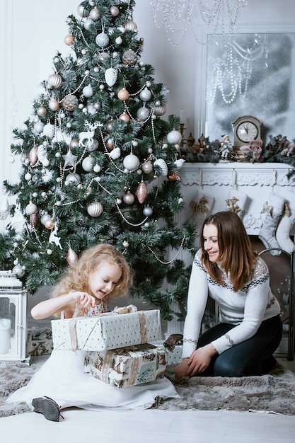 Madre e hija abren regalos bajo el árbol de navidad.