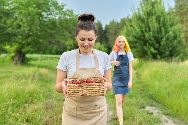 Madre e hija adolescente caminando junto con una cesta de fresas frescas