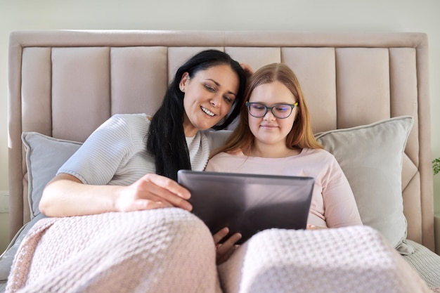 Madre e hija adolescente descansan juntas en casa usando una tableta digital