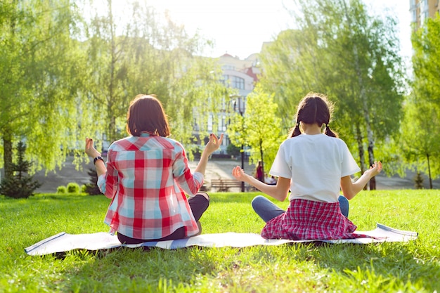 Madre e hija adolescente practicando yoga en el parque