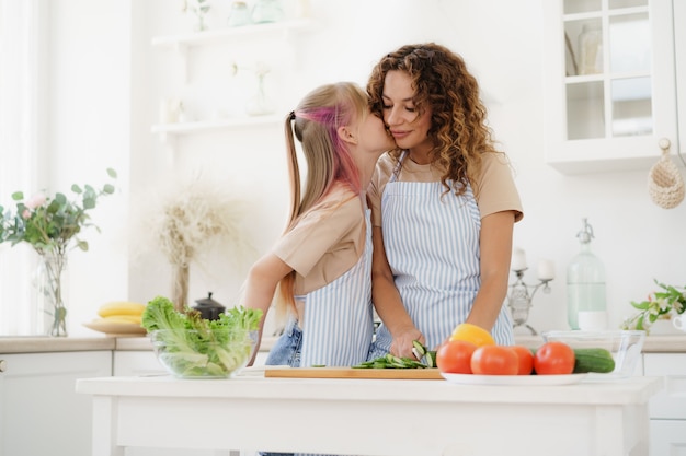 Madre e hija adolescente preparando ensalada de verduras en la cocina