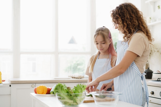 Madre e hija adolescente preparando ensalada de verduras en la cocina