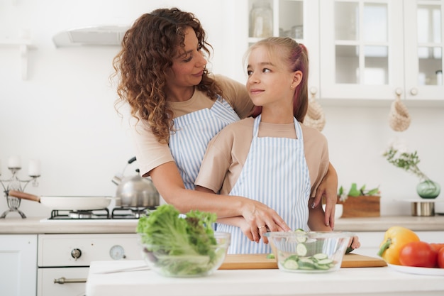 Madre e hija adolescente preparando ensalada de verduras en la cocina