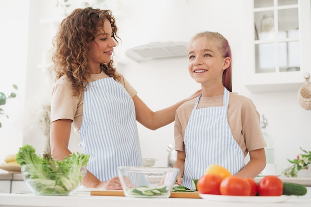 Foto madre e hija adolescente preparando ensalada de verduras en la cocina