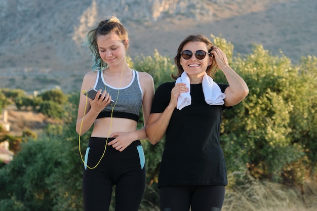 Madre e hija adolescente en ropa deportiva haciendo fitness juntos, camino de montaña de naturaleza puesta de sol de fondo