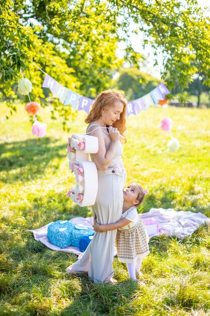 Madre e hija alegres que se divierten en el cumpleaños del niño en una manta con adornos de papel en el parque