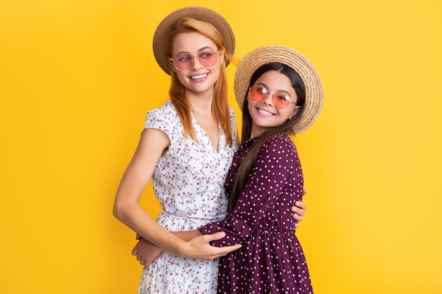 Madre e hija alegres con sombrero de paja sobre fondo amarillo