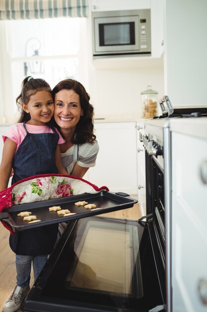 Foto madre e hija con bandeja de galletas horneadas en la cocina