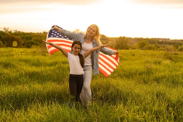 Madre e hija con bandera estadounidense en un hermoso campo.