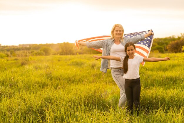 Madre e hija con bandera estadounidense en un hermoso campo.