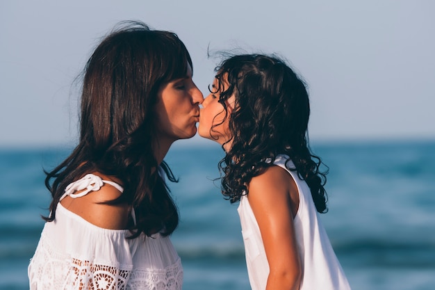 Foto madre e hija se besan en la playa